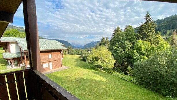 A wooden cabin with a balcony overlooking a lush green landscape and mountains in the distance. - Simple duplex with parking in La Clusaz (La Clusaz)