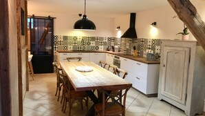 A kitchen with a wooden table and chairs, a tiled backsplash, and a black range hood. - The 2 Alpes / Venosc, 10 pers. NEW with steam room, sauna, jacuzzi. (les deux alpes)