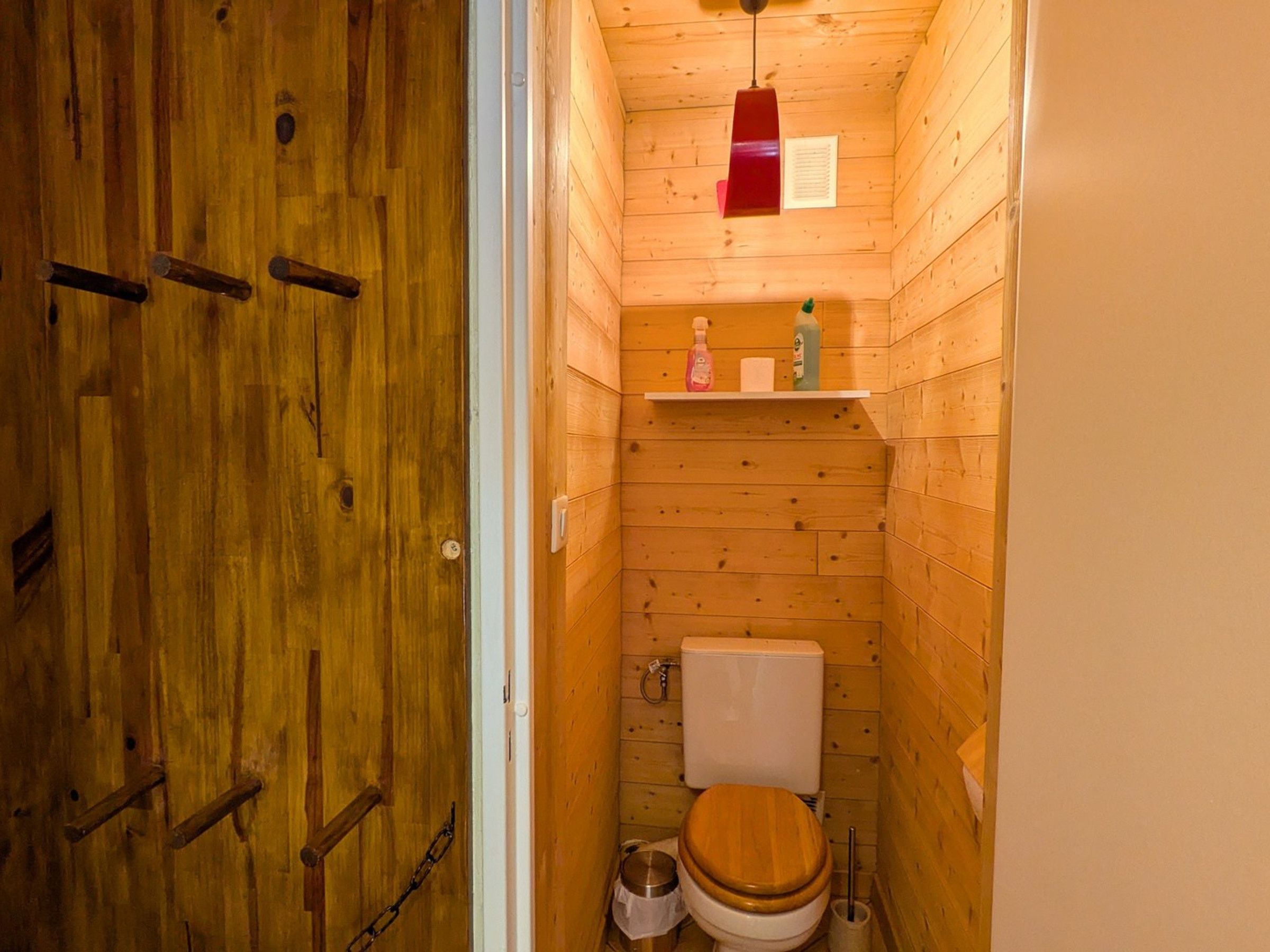 Une petite salle de bain en bois, avec des toilettes, une étagère contenant des articles de toilette et une porte en bois.