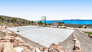 A basketball court with a net, surrounded by rocks and a house in the background.