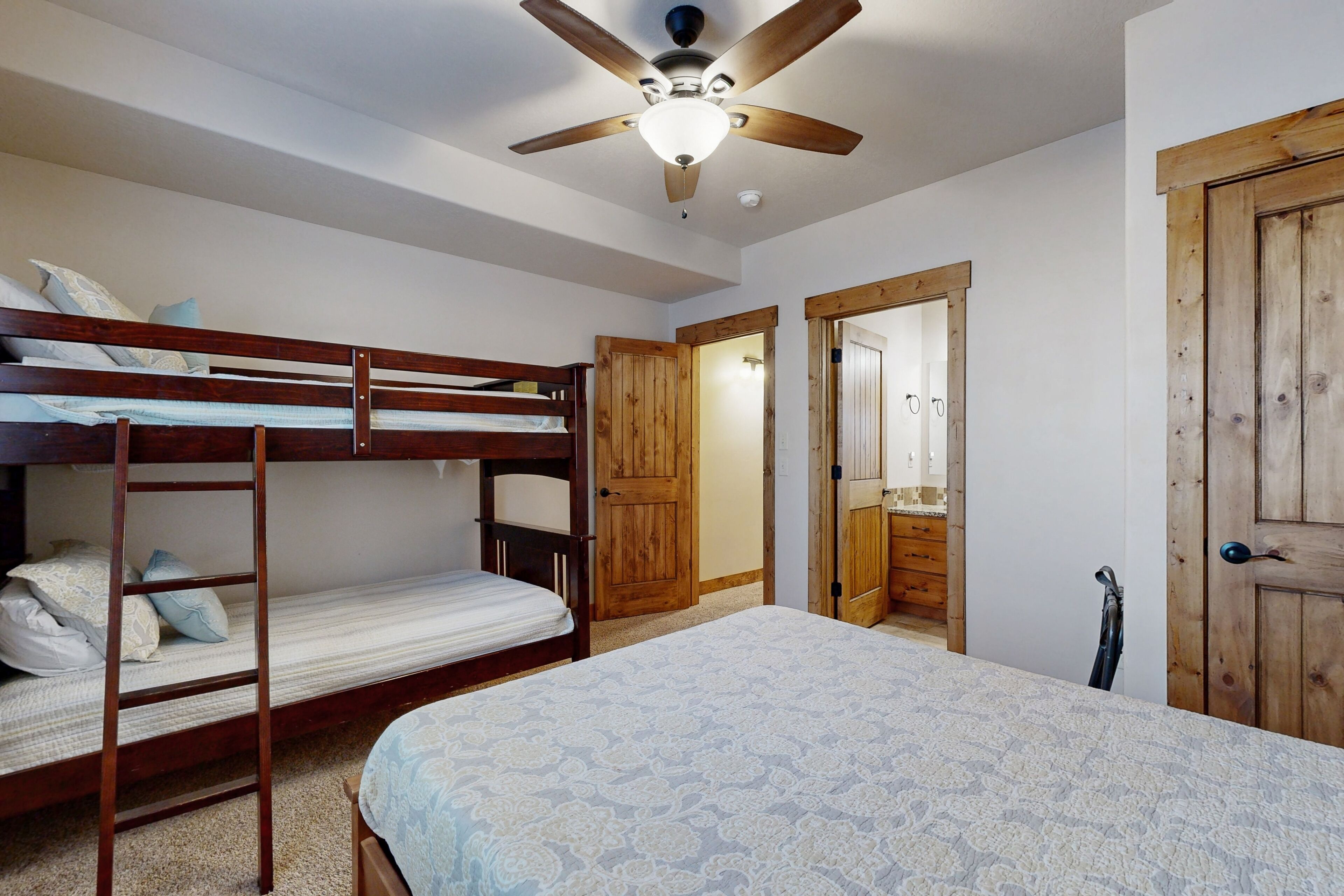 Une chambre avec des lits superposés, un ventilateur de plafond et des portes en bois.