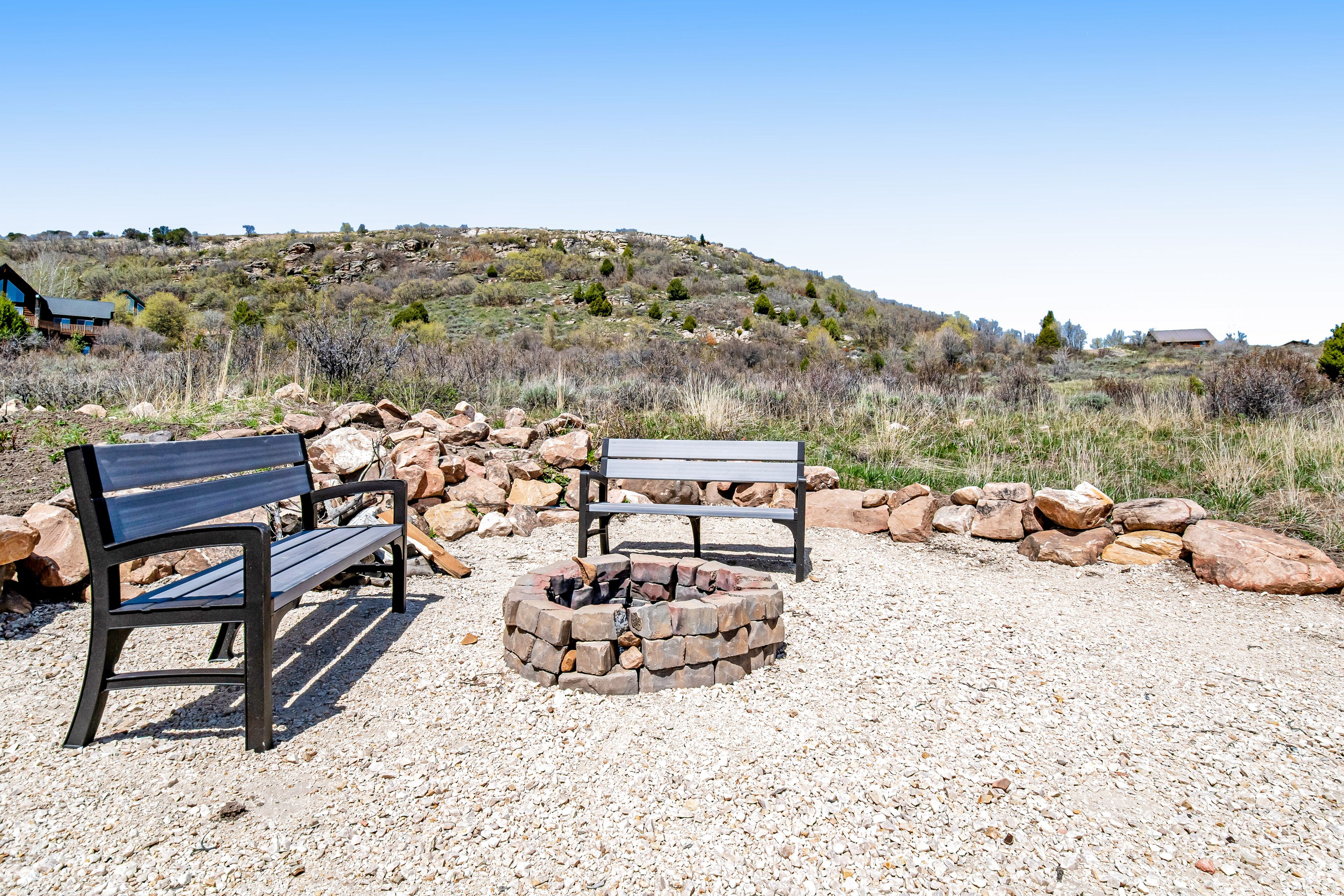 Two benches and a fire pit in a rocky outdoor area with a hilly landscape in the background.