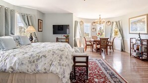 Une chambre spacieuse avec un grand lit, un coin repas agrémenté d’un lustre, et un téléviseur fixé au mur.
