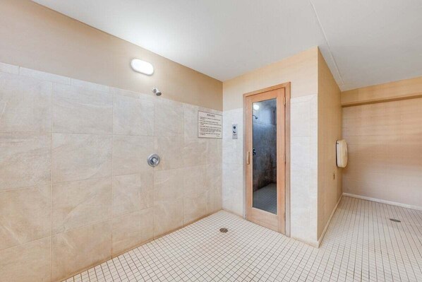 Un área de ducha con paredes y suelo de azulejos, una puerta de madera y un secador de manos.