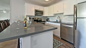 Una cocina moderna con armarios blancos, electrodomésticos de acero inoxidable y una isla central con una botella de vino y una copa.