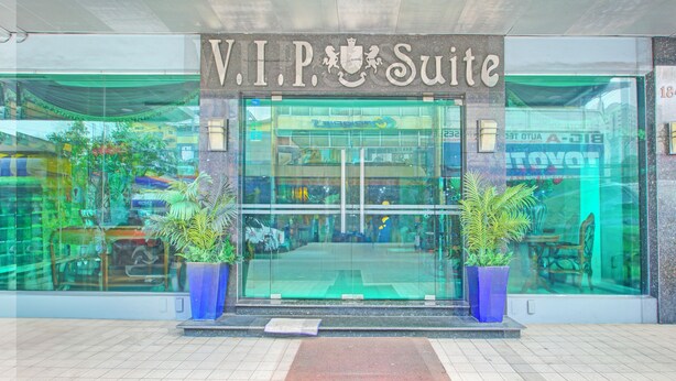 Exterior de un hotel V.I.P. Suite con fachada de vidrio, dos plantas en macetas y un área de entrada con baldosas.