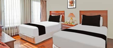 Habitación de hotel con dos camas, una mesita de noche con lámpara, un cuadro enmarcado en la pared y una ventana con cortinas.