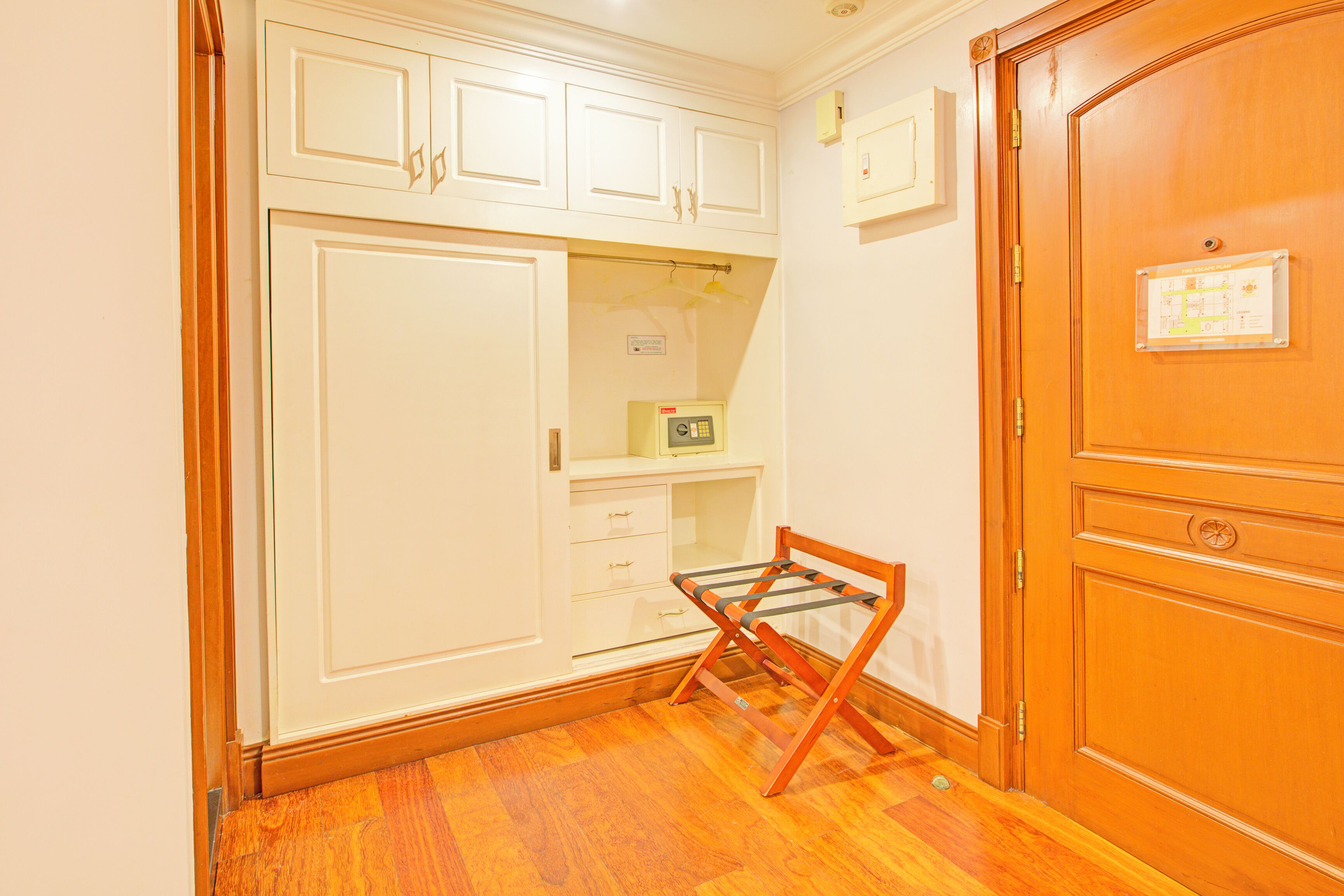A room with a wooden floor, white cabinets, a wooden door, and a small table with a chair.