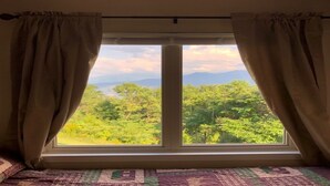 Ein Schlafzimmer mit großem Fenster, Vorhängen und einem Bett mit gemustertem Bettbezug.