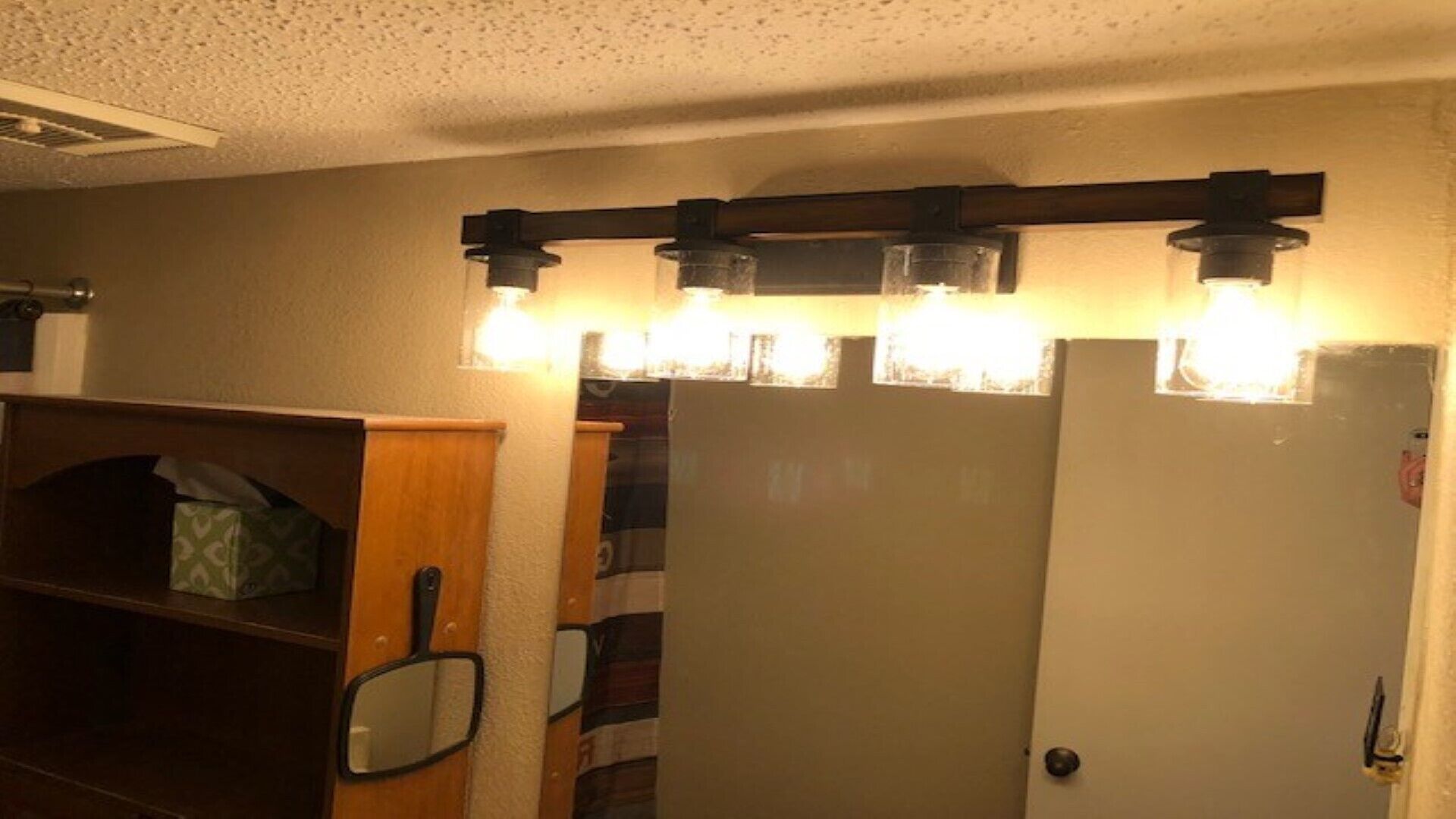 Una habitación con estante de madera, un espejo y una puerta blanca con una lámpara arriba.