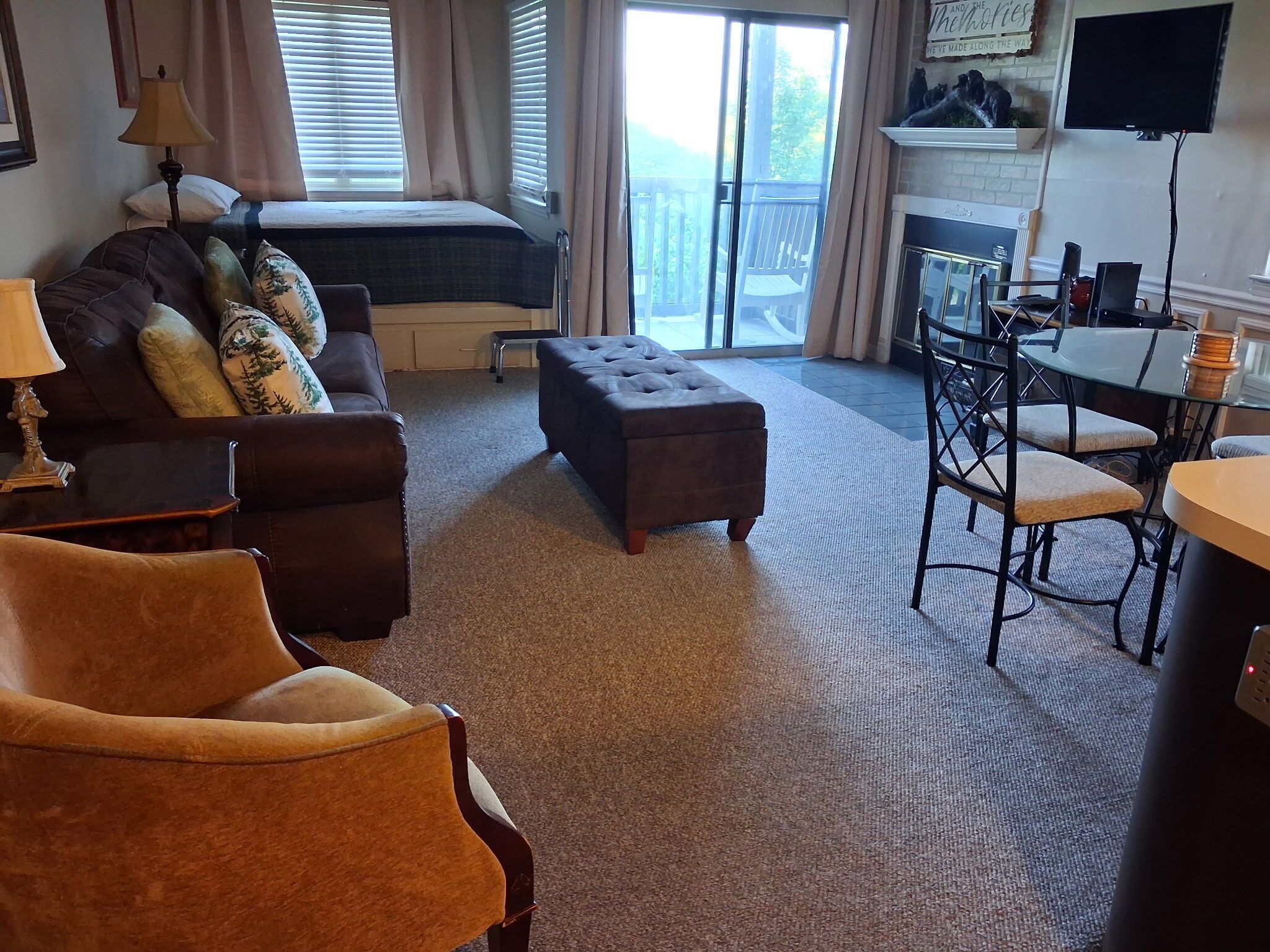 A hotel room with a bed, a sofa, an ottoman, a dining table with chairs, and a television.