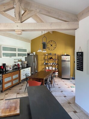 Une cuisine avec un plafond en bois, une horloge noire et un tableau noir où sont inscrites les tâches quotidiennes.