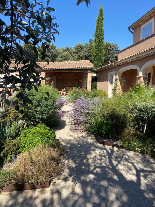 Un sentier de jardin menant à un bâtiment doté d’un toit en tuiles et d’arcades.