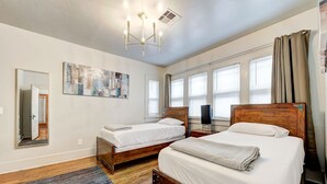 Ein Hotelzimmer mit zwei Betten, einem großen Fenster mit Jalousien, einer Deckenleuchte und einem Bild an der Wand.