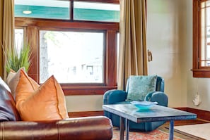 A room with a wooden-framed window, a blue sofa, and a small table with a blue bowl. - Classen Craftsman-near Asian & Paseo district (Oklahoma City)