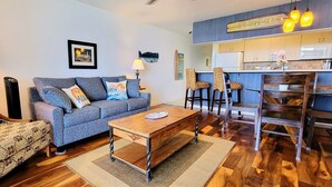 Una sala de estar con sofá, sillones, una mesa de centro y una zona de comedor con taburetes de bar.