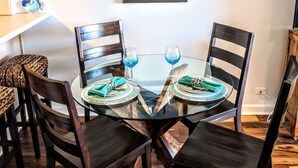 Un comedor con una mesa redonda de vidrio, sillas de madera oscura y lámparas colgantes naranjas.