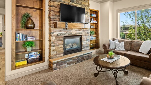 A living room with a stone fireplace, a flat-screen TV mounted above it, and a ceiling fan. - St. George Gem, Pool, Hot Tub, View, Zion Basecamp (Hurricane)
