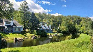 A serene lakeside property with two houses, a well-maintained lawn, and a calm pond. - Village 43 | Spacious End Unit with Loft, Fireplace & Resort Amenities (Killington)