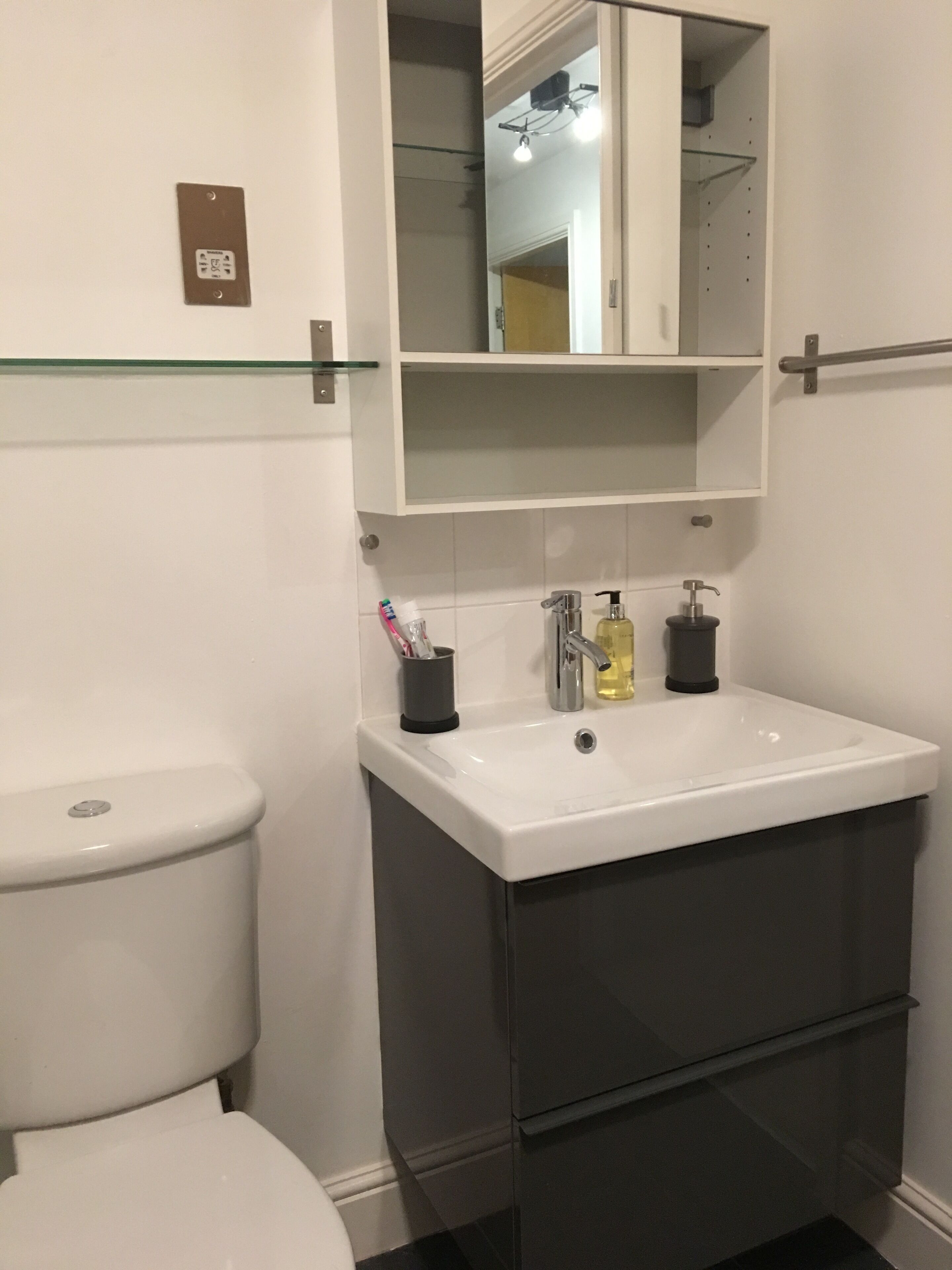 A modern bathroom with a white toilet, a white sink with a mirror above it, and a dark-colored cabinet below.