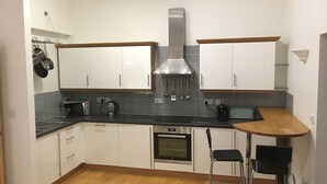 Una cocina moderna con armarios blancos, una campana extractora de acero inoxidable, un microondas y un horno empotrado. Hay dos taburetes de bar y una pequeña isla con un lavamanos.
