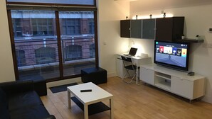 Una sala de estar moderna con un sofá, una mesa de centro, un escritorio con una computadora portátil y un televisor sobre un mueble.