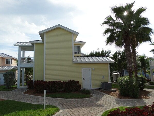 A yellow building with a flat roof, a small porch, and a palm tree nearby. - Rent a 2 bed / 2 bath Villa in Alice Town, North Bimini (INCLUDES 50' dock slip) (North Bimini)
