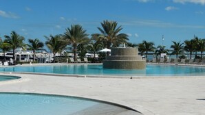 A swimming pool with a circular stone feature, palm trees, and a clear blue sky.