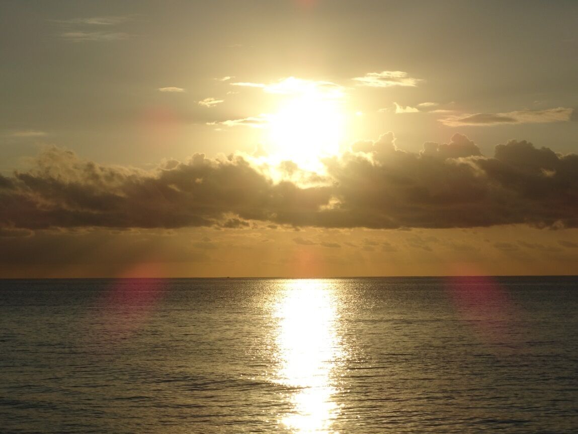 A sunset over a calm sea with clouds reflecting the sunlight.