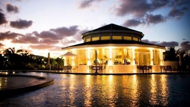A circular building with a covered patio area, surrounded by water reflecting the structure.