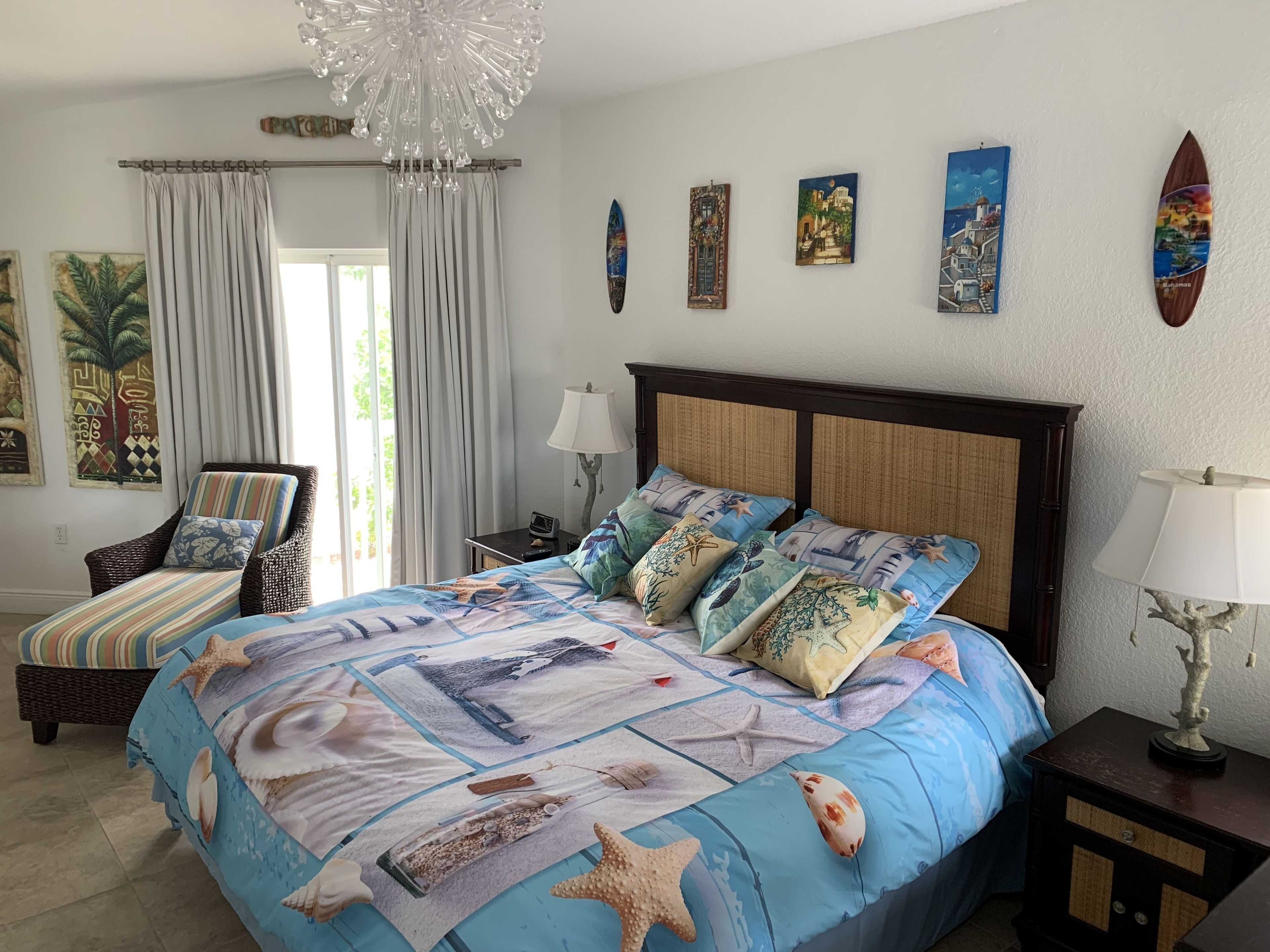 A bedroom with a large bed, a chair, a nightstand, and a wall with paintings.