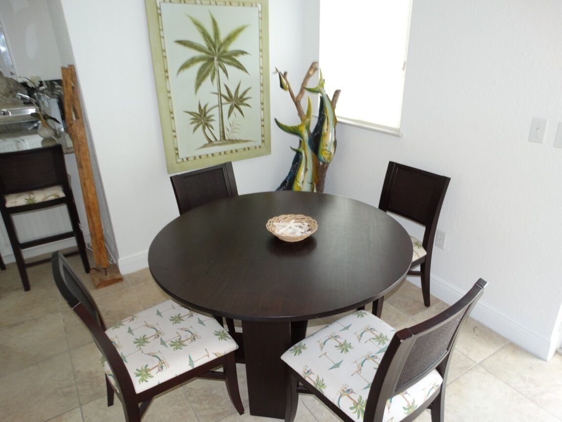 A round dining table with four chairs, each with a patterned cushion. A woven basket is placed on the table.