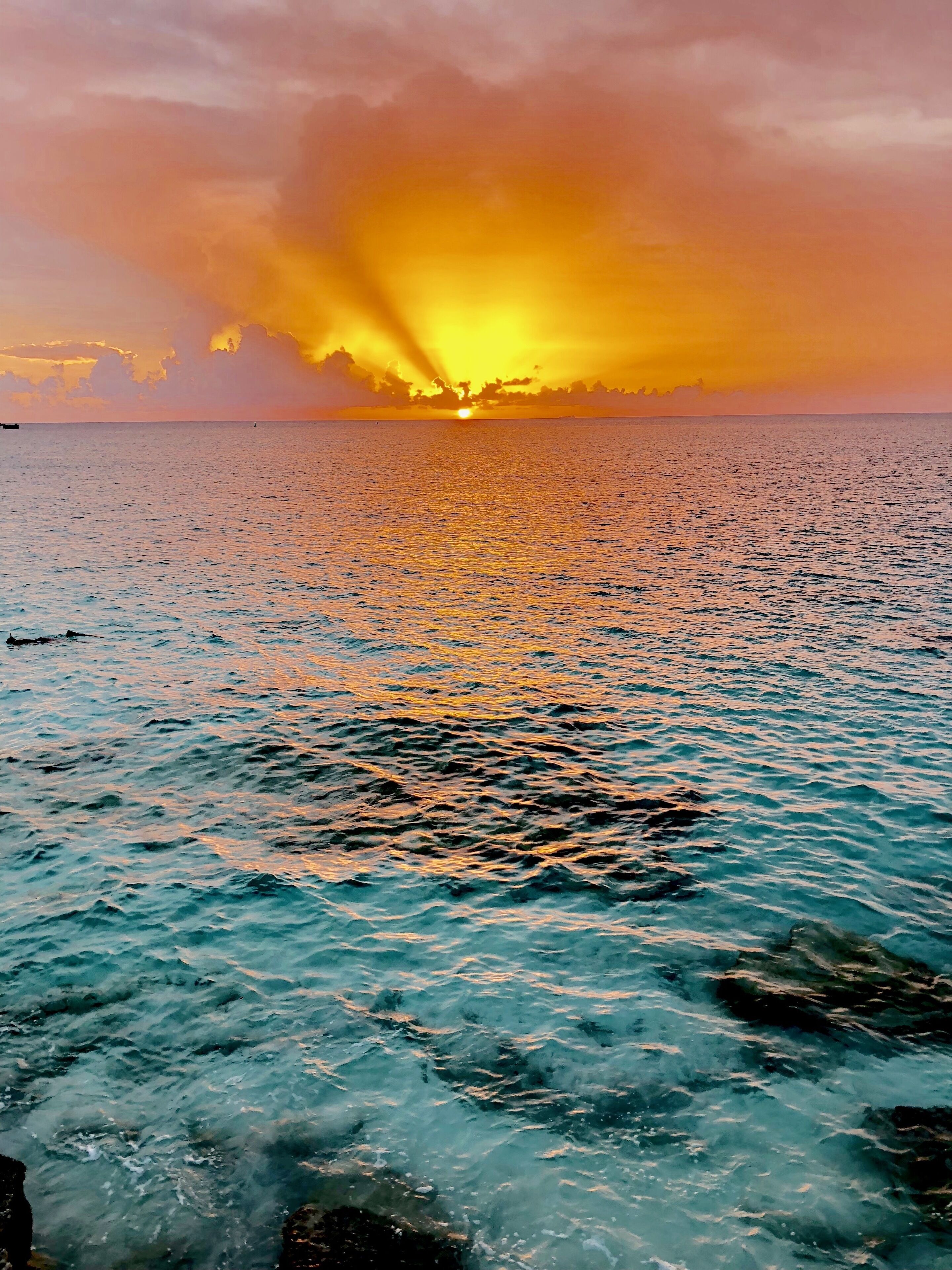 A sunset over a calm sea with a rocky shoreline.