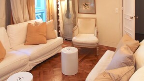 A living room with a white sofa, a white armchair, a wooden floor, a chandelier, a lamp, and framed pictures on the wall. - Elegance in Saint Germain des Prés - Bonaparte - Left Bank (Paris)