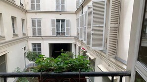 A courtyard with a balcony railing, potted plants, and a building facade with shutters. - Elegance in Saint Germain des Prés - Bonaparte - Left Bank (Paris)