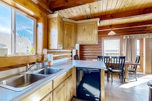 A kitchen with wooden cabinets, a dishwasher, a sink, and a dining area with chairs and a table.