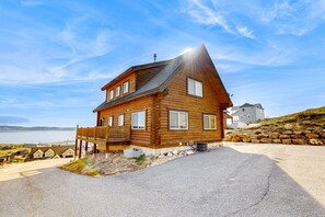 A wooden cabin with a sloped roof, a deck, and a view of the water. - Beautiful log cabin with lake views, wraparound deck, & foosball (Garden City)
