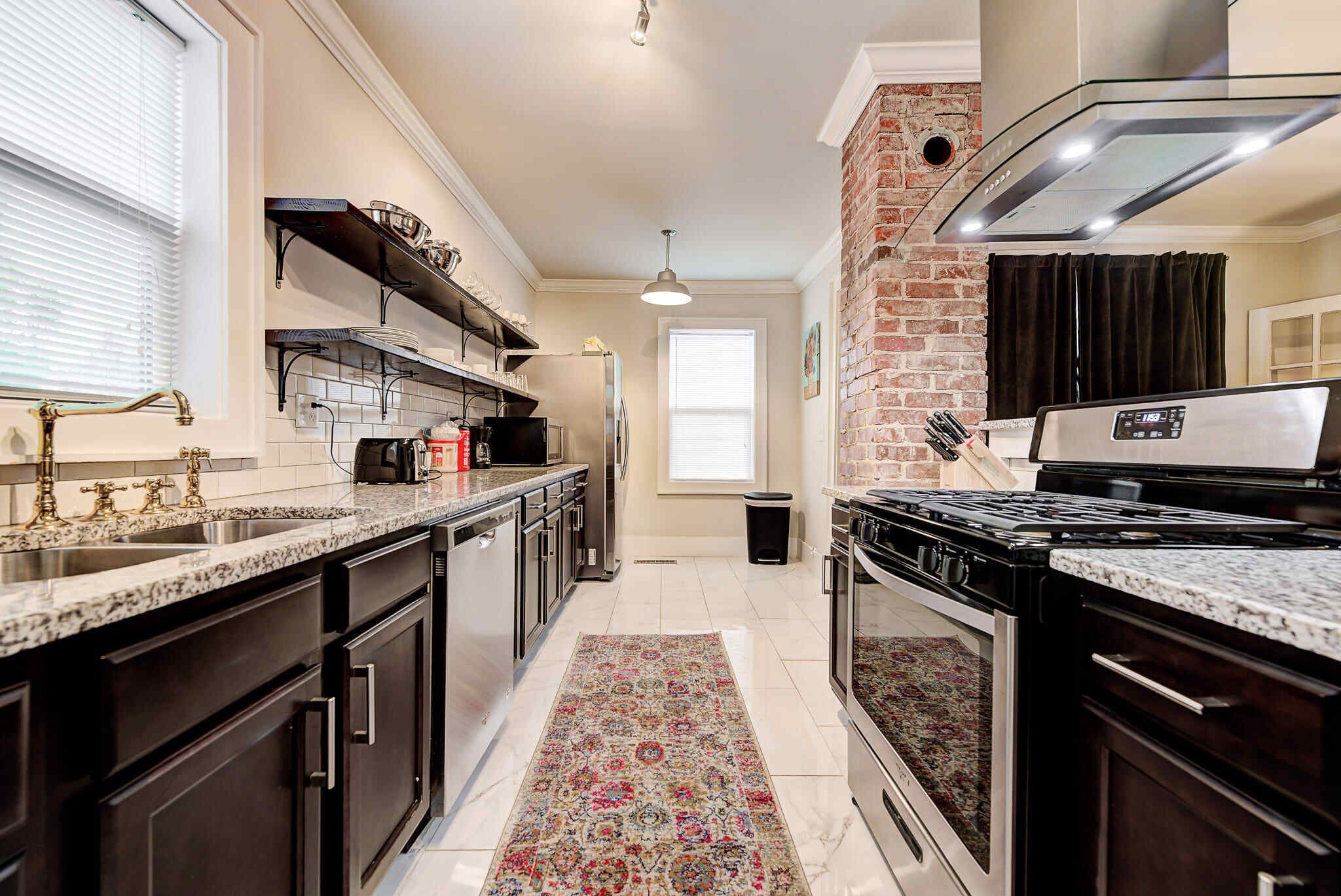 A kitchen with granite countertops, stainless steel appliances, and a patterned rug.