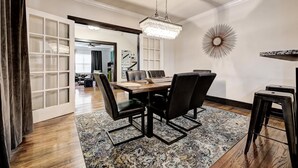 A dining area with a wooden table, black chairs, a patterned rug, a chandelier, and a decorative wall piece. - Howes Capitol II-Sleek & spacious-walk to OU Med (Oklahoma City)