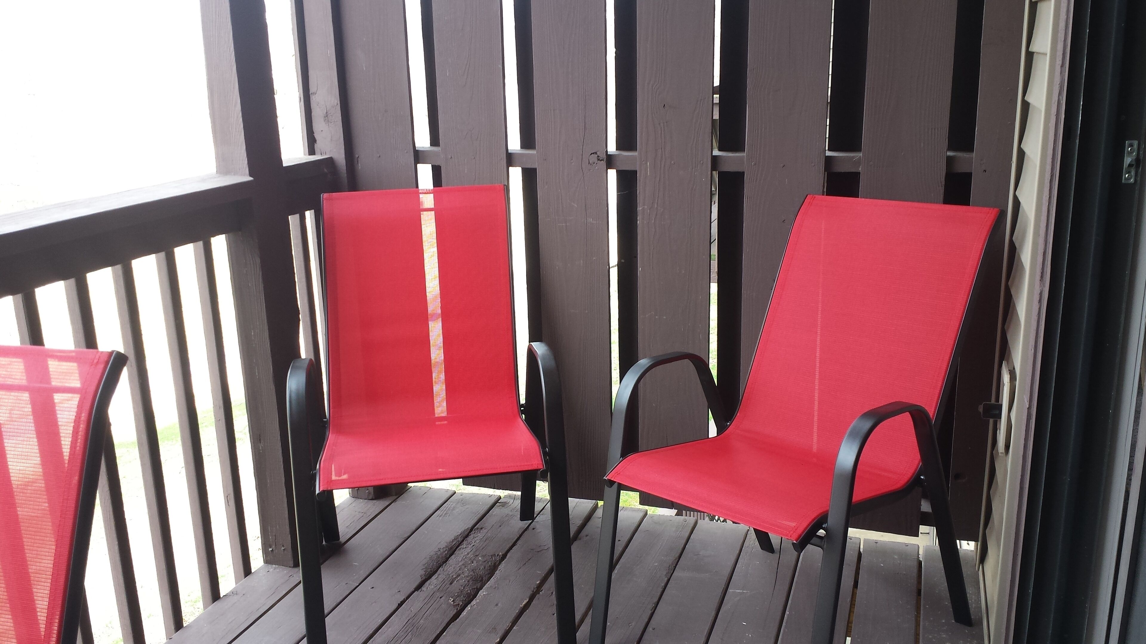 Two red chairs with black frames on a wooden deck.