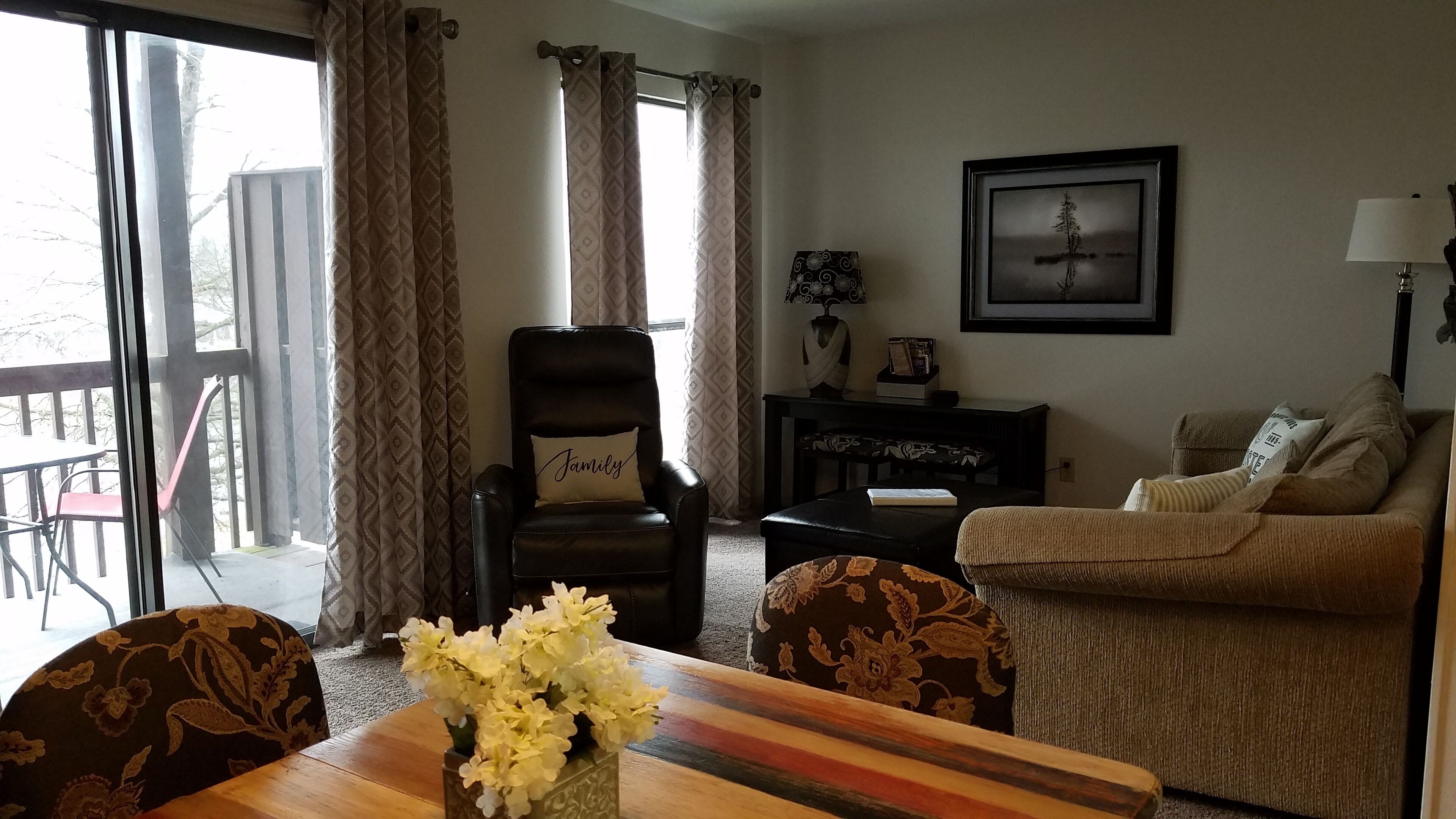 A living room with a sofa, a chair, a table with a vase of flowers, a lamp, and a framed picture on the wall.