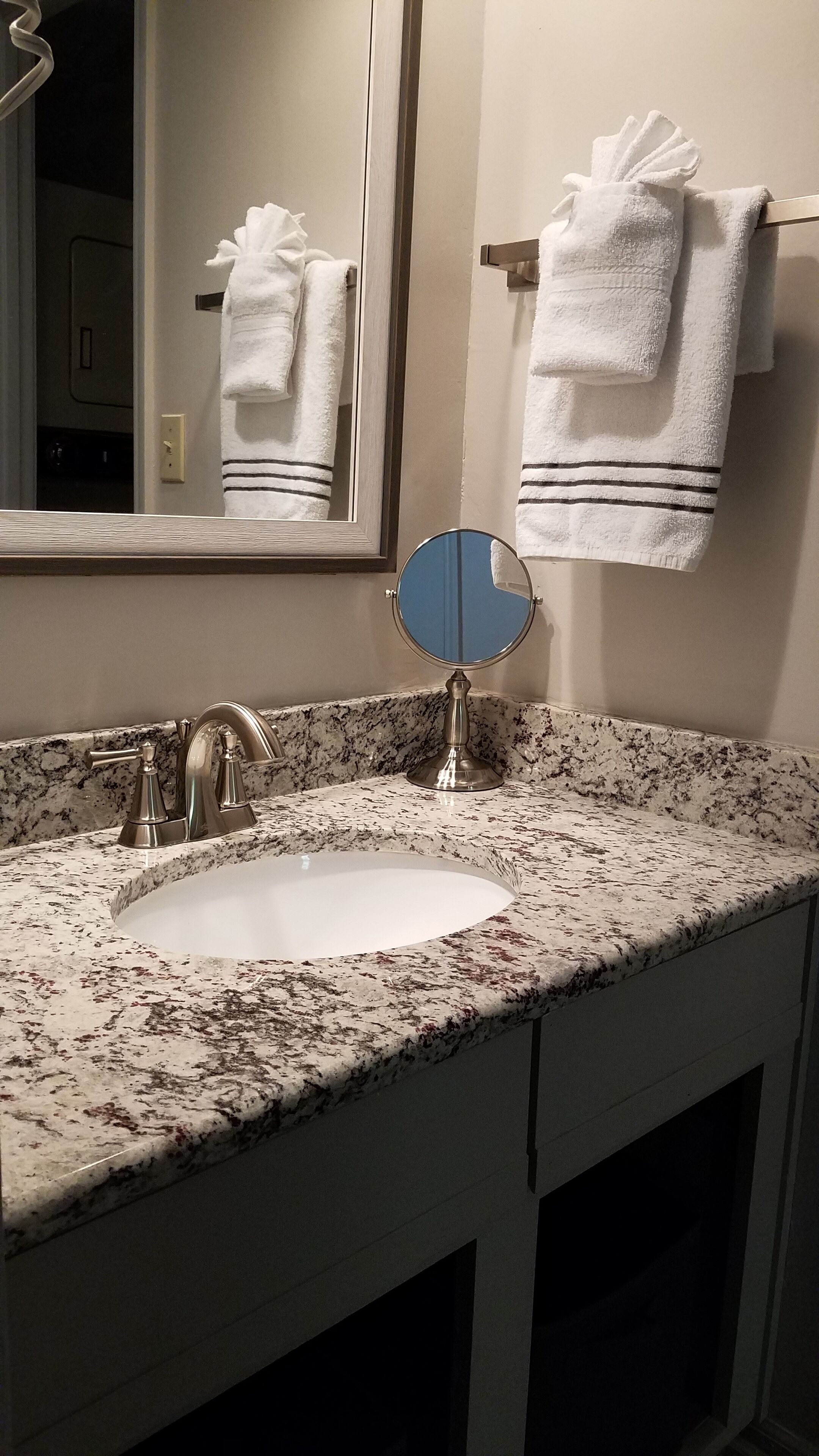 Une salle de bain avec un lavabo doté d’un plan de travail en granit, un miroir et deux serviettes accrochées au mur.