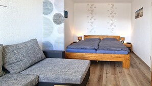 A bedroom with a wooden bed, a grey sofa, and patterned walls.