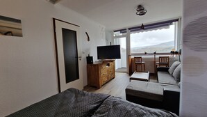 A living room with a sofa, a TV on a wooden cabinet, a small table, and a view of the outdoors through a window.