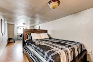 A bedroom with a bed, a wooden headboard, a ceiling light, and a view of a hallway.