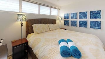 A hotel room with a bed, two bedside lamps, a ceiling fan, a window with blinds, and six framed pictures on the wall.