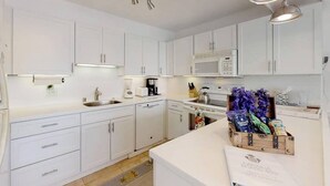 A modern kitchen with white cabinets, a microwave, a coffee maker, and a wooden crate with items on the counter. - Perfect location and Unbelievable Views at Lahaina Roads (Lahaina)