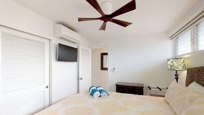 A bedroom with a bed, a ceiling fan, a TV, a bedside table, and a lamp. - Perfect location and Unbelievable Views at Lahaina Roads (Lahaina)