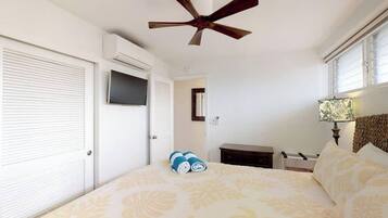 A bedroom with a bed, a ceiling fan, a TV, a bedside table, and a lamp.