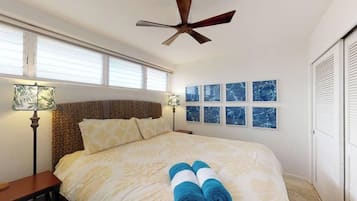 Una camera d'albergo con un letto, una ventola a soffitto, un comodino, una lampada e una finestra con tende.